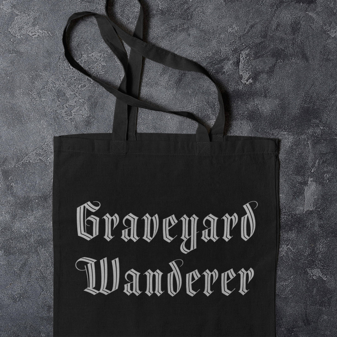 Black tote bag with 'Graveyard Wanderer' text on a textured gray background