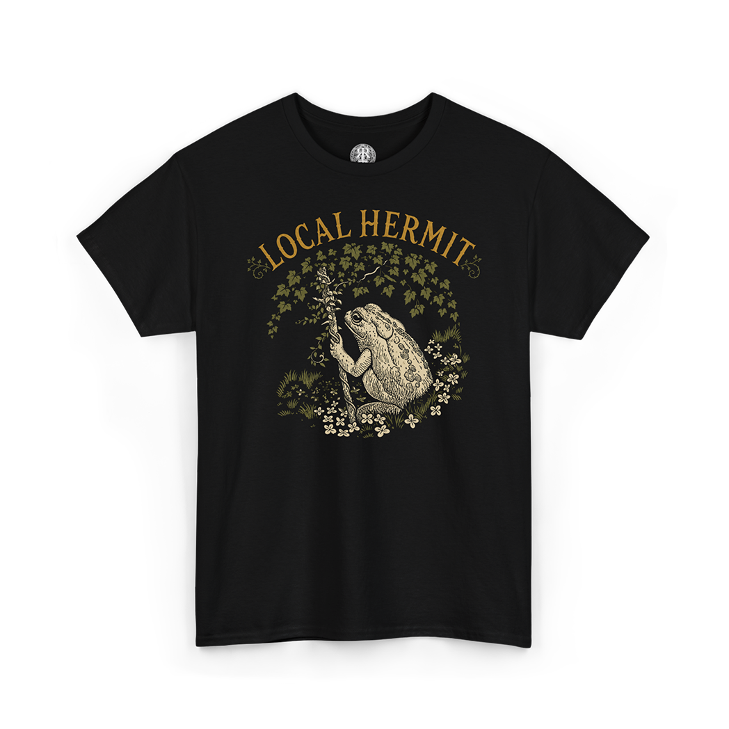 A black short-sleeve crewneck t-shirt featuring a vintage-style graphic of a toad holding a staff, surrounded by flowers and leaves, with the text 'LOCAL HERMIT' printed above in a warm tan color.