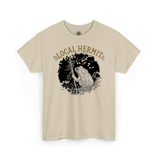 A beige short-sleeve crewneck t-shirt featuring a graphic print of a toad in a black circle with the text 'LOCAL HERMIT' in tan above it, displayed on a clean white background.