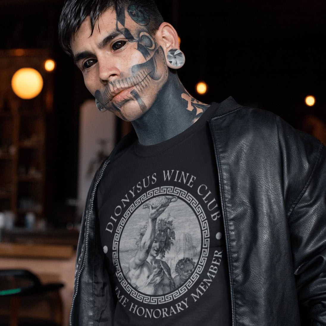 Person wearing a black leather jacket with a Dionysus Wine Club t-shirt in a dimly lit setting.