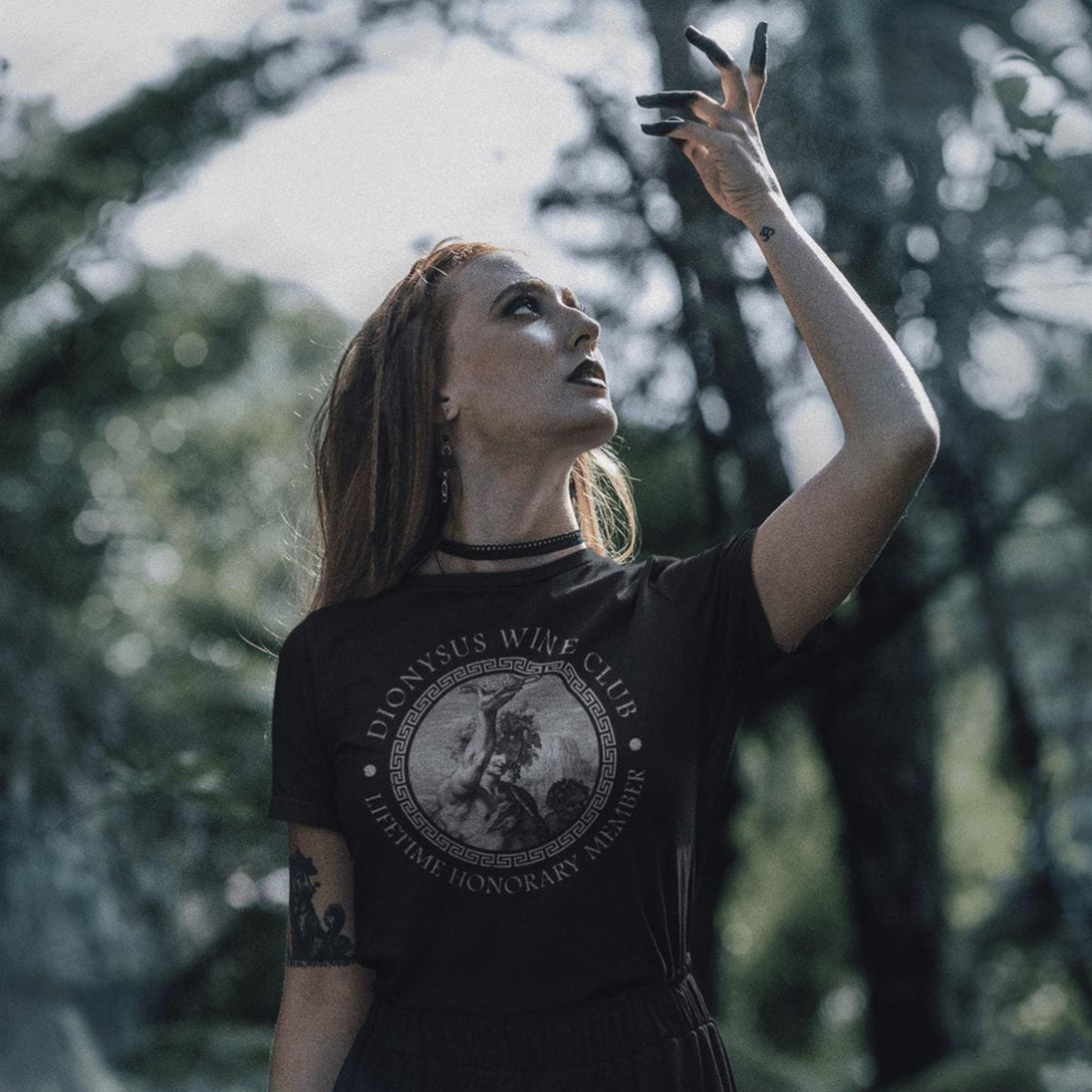 Woman wearing a black leather jacket with a Dionysus Wine Club t-shirt in a forest.