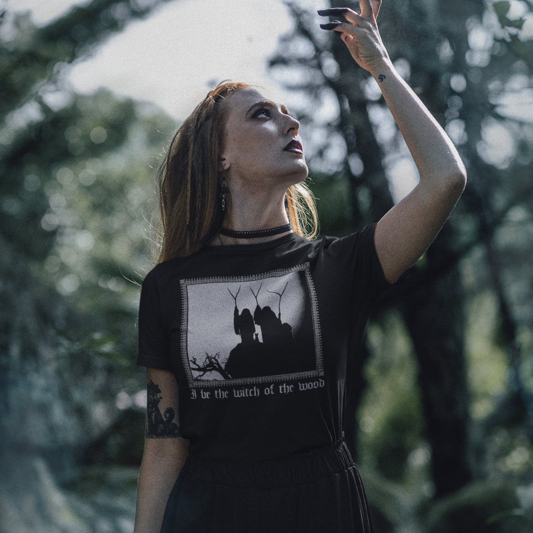 Woman in a black t-shirt with a graphic design of three witches of macbeth in a forest