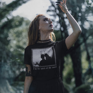 Woman in a black t-shirt with a graphic design of three witches of macbeth in a forest