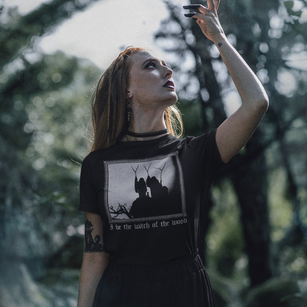 Woman in a black t-shirt with a graphic design of three witches of macbeth in a forest