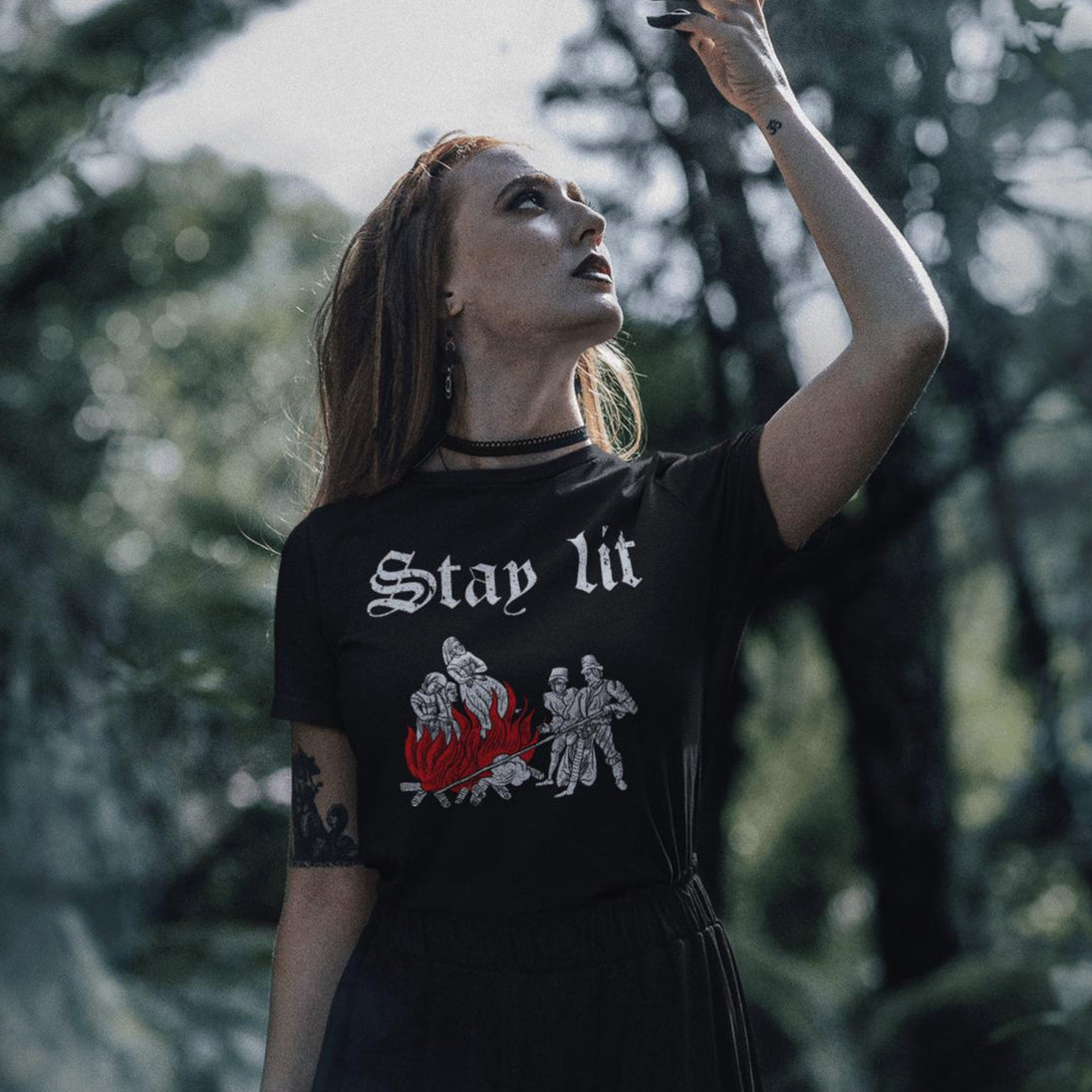 Woman wearing a black t-shirt with 'Stay Lit' design in a forest setting