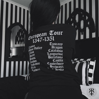 Person wearing a black t-shirt with a European tour itinerary printed on the back, sitting in a room with striped walls.