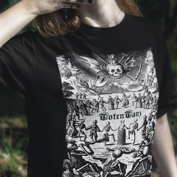 Person wearing a black t-shirt with a graphic design of skeletons dancing and a skull with a scythe.