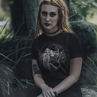 Woman wearing a black Rapunzel T-Shirt, sitting in a forest setting.