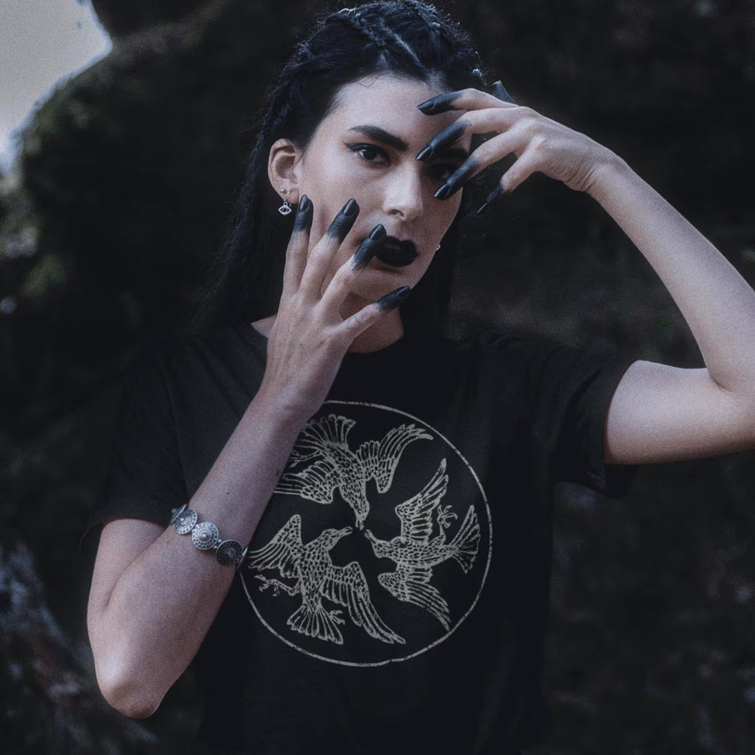 Person wearing a black t-shirt with a bird design, posing with hands on face.