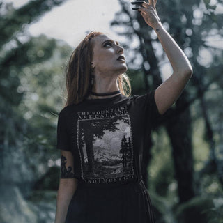 Woman in forest setting wearing black The Mountains Are Calling And I Must Go T-Shirt