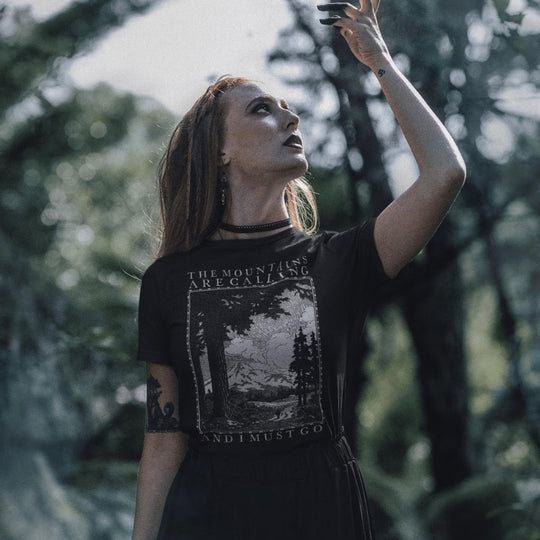 Woman in forest setting wearing black The Mountains Are Calling And I Must Go T-Shirt