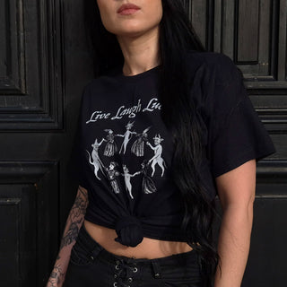 Woman wearing a black t-shirt with white graphic design of witches dancing with the devils and saying LIVE LAUGH LUCIFER above