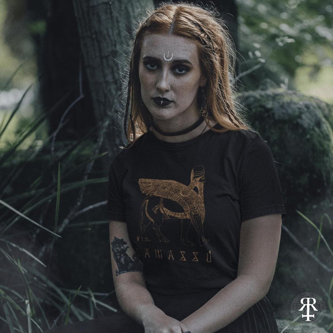 Person wearing a black t-shirt with lamassu winged lion design in a forest setting