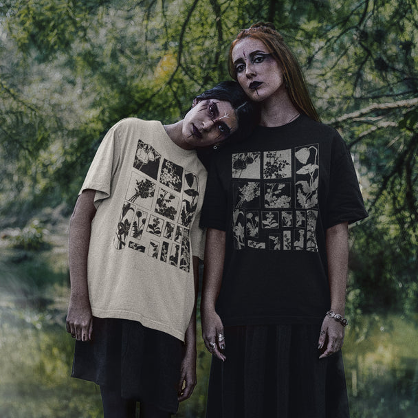 Two models posing outdoors in front of a blurred forest background, wearing graphic t-shirts. The model on the left wears a beige t-shirt with a black graphic print, and the model on the right wears a black t-shirt with a white graphic print.