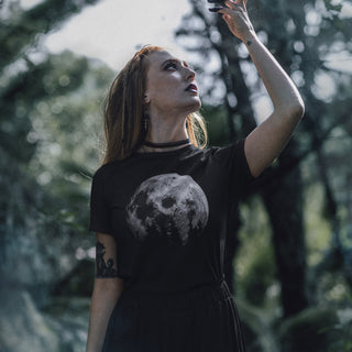 Woman in a black t-shirt with a moon design, standing in a forest.