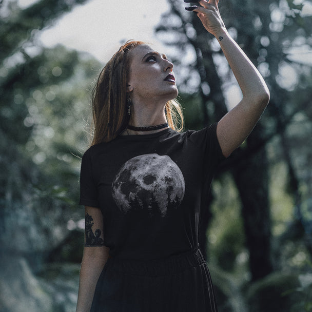Woman in a black t-shirt with a moon design, standing in a forest.