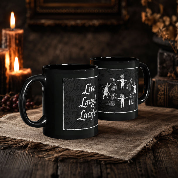 Two black ceramic mugs with white printed designs, displayed on a rustic burlap cloth with candles and a dark wooden table in the background.