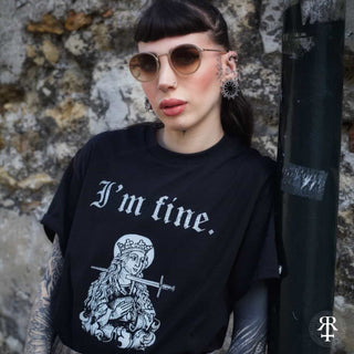Person wearing a black t-shirt with 'I'm fine.' text and graphic design, standing against a stone wall.