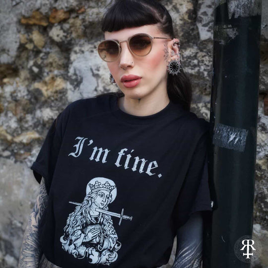 Person wearing a black t-shirt with 'I'm fine.' text and graphic design, standing against a stone wall.