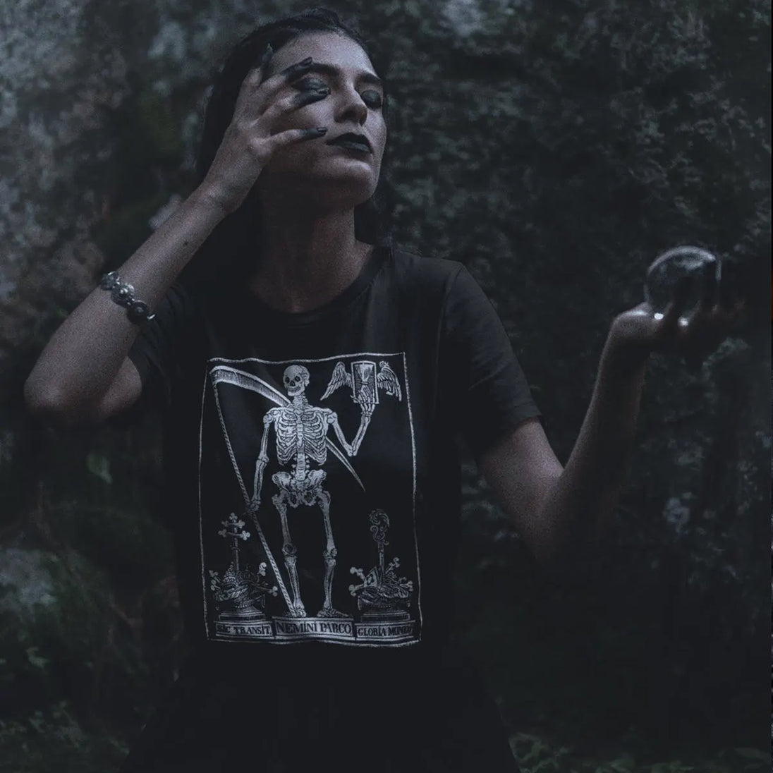 Person wearing a black t-shirt with a skeleton design in a dark, forest-like setting