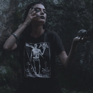 Person wearing a black t-shirt with a skeleton design in a dark, forest-like setting