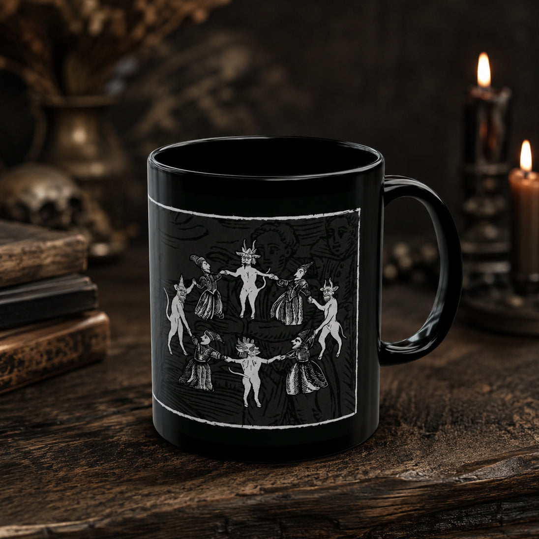 A black ceramic mug with a white gothic illustration of dancing figures, displayed on a rustic wooden table with candles and books in the background.
