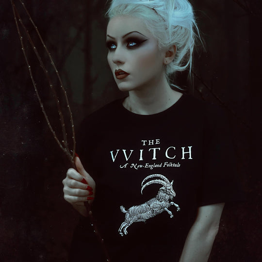 Person wearing a black t-shirt with 'The Wwitch' logo holding a branch in a dark setting