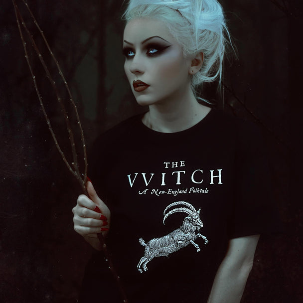 Person wearing a black t-shirt with 'The Wwitch' logo holding a branch in a dark setting